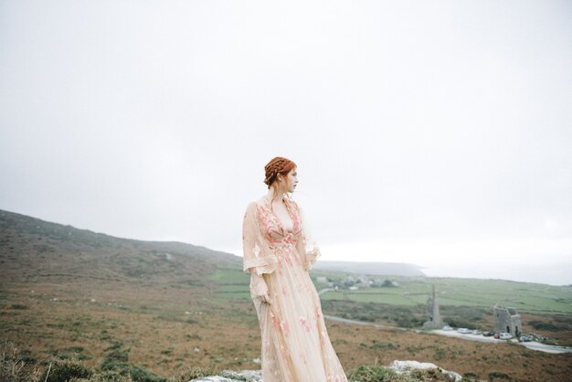 Linda foto vertical de uma mulher ruiva com pele totalmente branca em um lindo vestido rosa