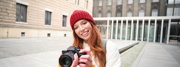 Linda fotógrafa readhead com câmera profissional tira fotos ao ar livre andando por aí