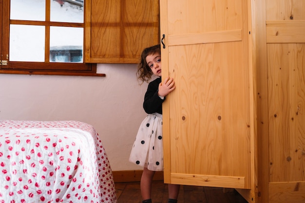Linda garota a espreitar do armário de madeira