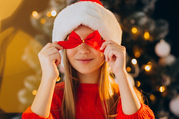 Linda garota adolescente com chapéu de Papai Noel vermelho perto da árvore de Natal