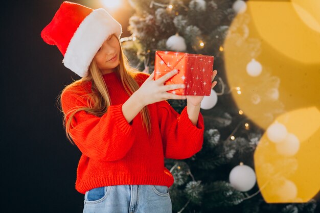 Linda garota adolescente com chapéu de Papai Noel vermelho perto da árvore de Natal