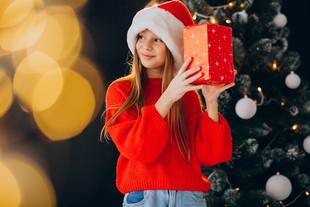 Linda garota adolescente com chapéu de Papai Noel vermelho perto da árvore de Natal