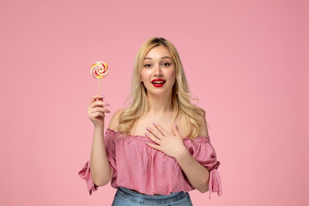 Linda garota adorável jovem com batom vermelho na blusa rosa em pé com pirulito e sorrindo