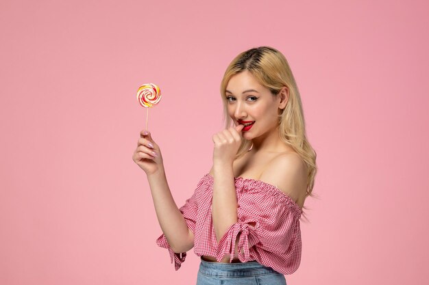 Linda garota adorável jovem com batom vermelho na blusa rosa mordendo o dedo segurando um doce