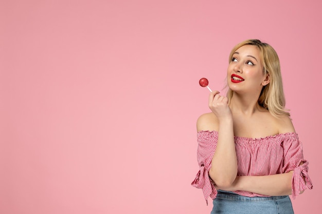 Linda garota adorável jovem com batom vermelho na blusa rosa olhando no ar segurando doces