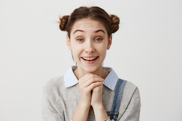 Linda garota adulta com penteado odango com sorriso segurando os punhos juntos. Mulher bonita emocionada que brilha com felicidade depois de receber a proposta de casamento. Expressões faciais