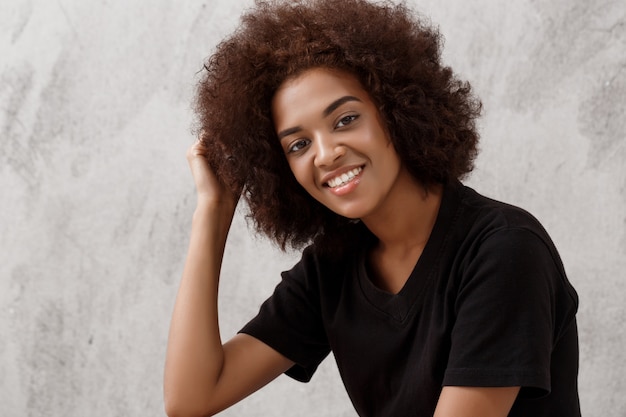 Foto grátis linda garota africana sentado e sorrindo sobre parede de luz.