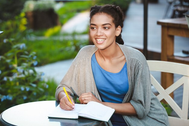 Linda garota africana sorridente, escrevendo no caderno