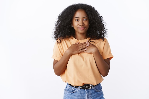 Linda garota afro-americana agradecida pressiona as palmas das mãos contra o peito como um gesto de agradecimento.