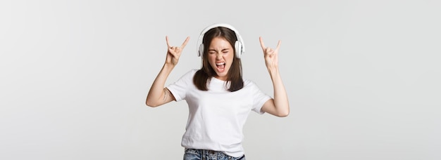 Foto grátis linda garota alegre em fones de ouvido dançando mostrando sinais de rocknroll