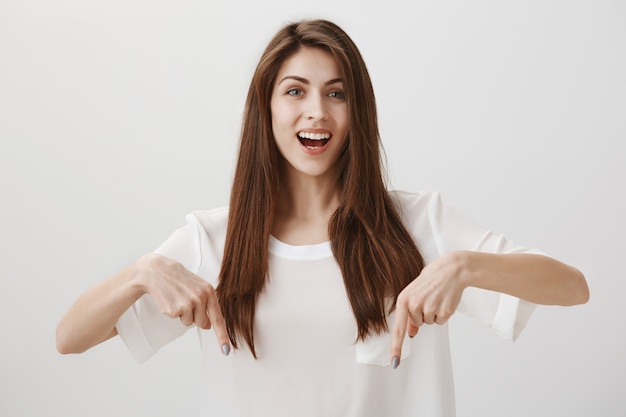 Foto grátis linda garota apontando o dedo para baixo para mostrar o anúncio, sorrindo feliz