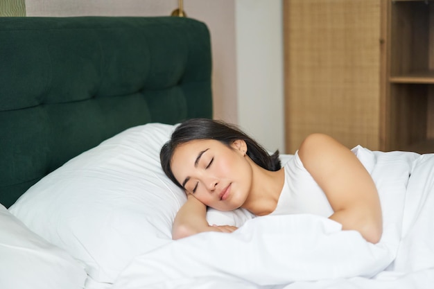 Linda garota asiática dorme em sua cama com lençóis brancos, edredom quente de inverno sorrindo em seu sonho de sono