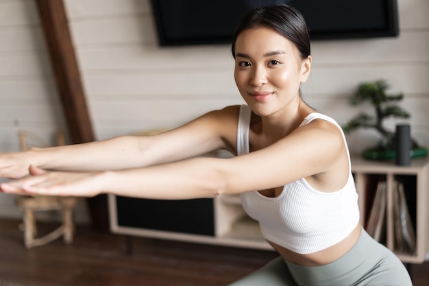 Linda garota asiática fitness em casa fazendo exercícios de agachamento com alongamento de corda elástica nas pernas dela exerci ...