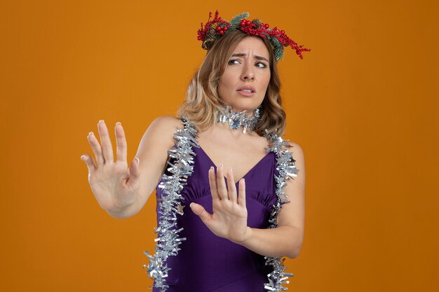 Linda garota assustada com um vestido roxo com uma coroa de flores estendendo as mãos ao lado, isolado em um fundo marrom