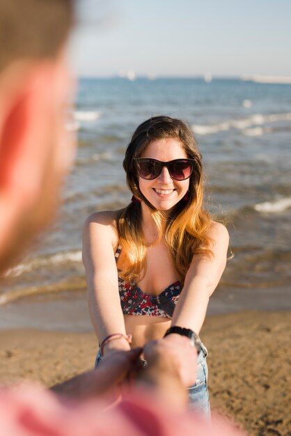 Linda garota atraente e alegre de mãos dadas com o namorado na praia