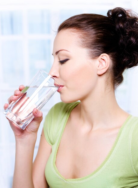 Linda garota bebe água de vidro - dentro de casa