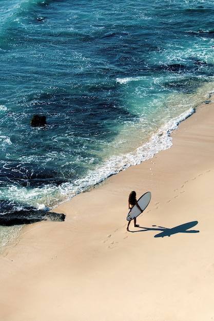 Foto grátis linda garota caminha com uma prancha de surf em uma praia selvagem. vista incrível do topo.