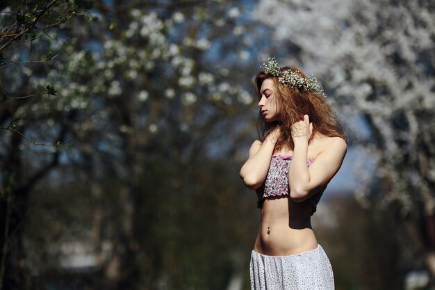 Linda garota caminha no exuberante jardim vestida com uma coroa de flores