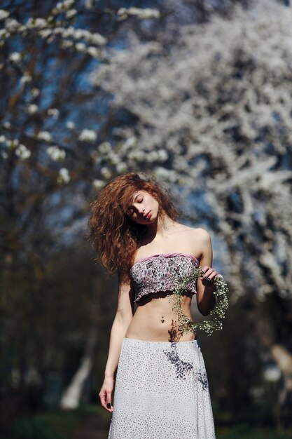 Linda garota caminha no exuberante jardim vestida com uma coroa de flores