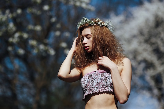 Linda garota caminha no exuberante jardim vestida com uma coroa de flores