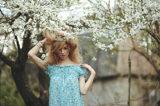 Linda garota caminha no exuberante jardim vestida com uma coroa de flores