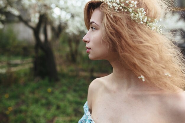 Linda garota caminha no exuberante jardim vestida com uma coroa de flores