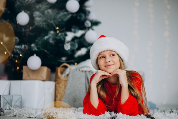 Linda garota com chapéu de papai noel debaixo da árvore de natal