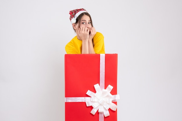 Linda garota com chapéu de papai noel em frente a um grande presente de natal