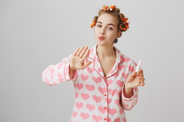 Linda garota com rolos de cabelo no cabelo e pijama, esmalte de unhas