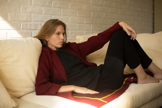 Linda garota com um casaco vermelho descansando no sofá