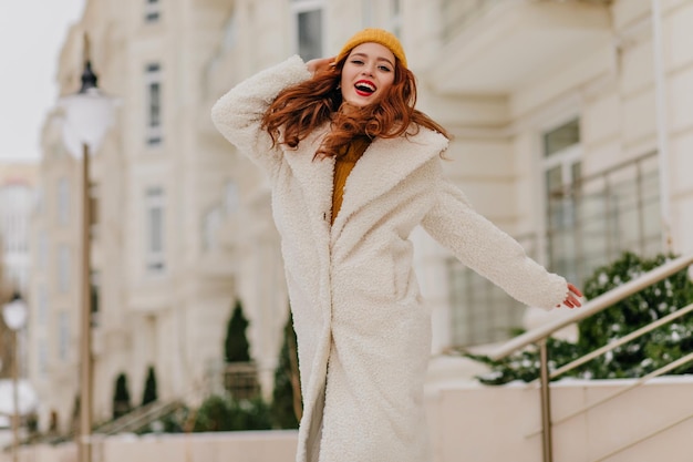 Linda garota com um lindo sorriso posando no inverno Foto ao ar livre da romântica senhora ruiva de casaco branco