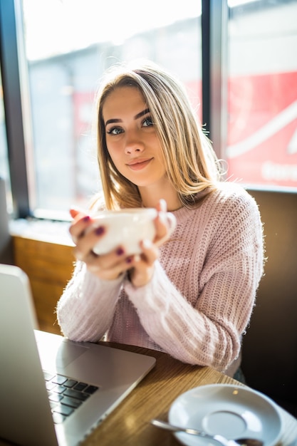 Linda garota com um suéter da moda, sentada em um café com uma xícara de chá, café, olhando para a câmera