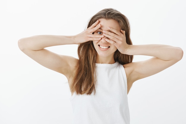 Linda garota curiosa espiando por entre os dedos enquanto fecha os olhos com as mãos