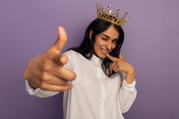 Linda garota curvada vestindo camiseta branca e coroa mostrando seu gesto isolado em roxo