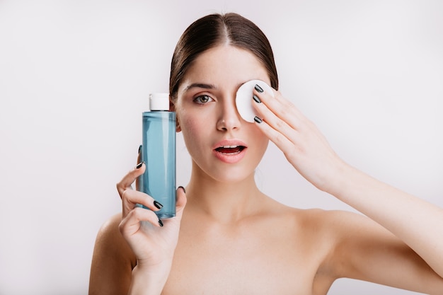Linda garota de olhos verdes passou uma esponja cosmética no rosto, removendo a sujeira. Retrato de uma mulher saudável sem maquiagem na parede branca.
