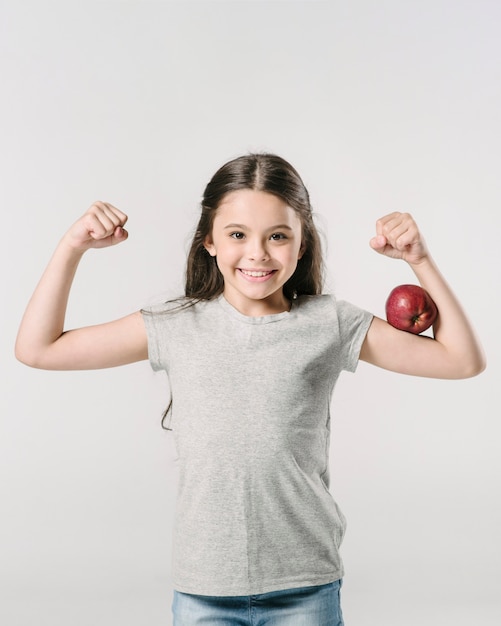 Linda garota de pé com a apple no bíceps em estúdio