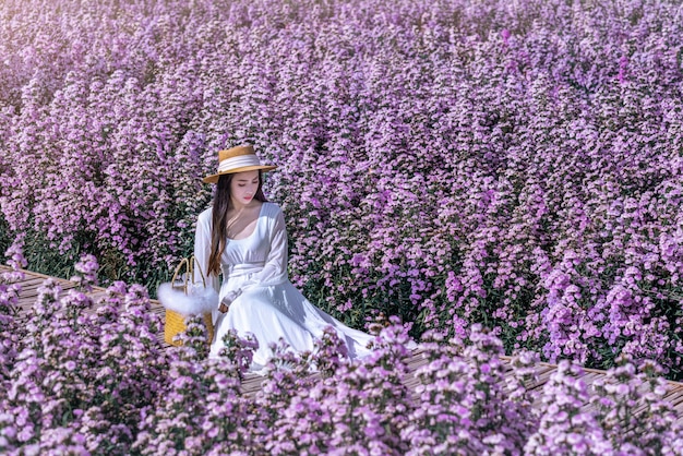 Linda garota de vestido branco sentada em um campo de flores de Margaret