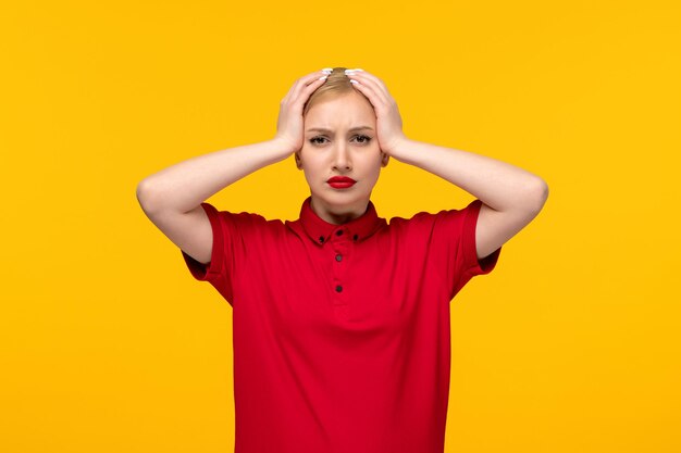 Linda garota do dia da camisa vermelha segurando a cabeça em uma camisa vermelha em um fundo amarelo