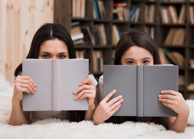 Linda garota e mulher cobrindo o rosto com livros