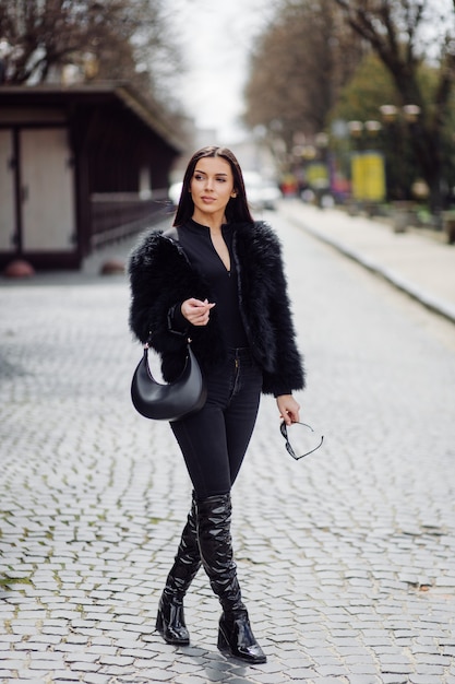 Linda garota elegante de cabelos castanhos em vestido preto ao ar livre. retrato de jovem atraente mulher elegante com cabelo comprido na primavera nas ruas da cidade.