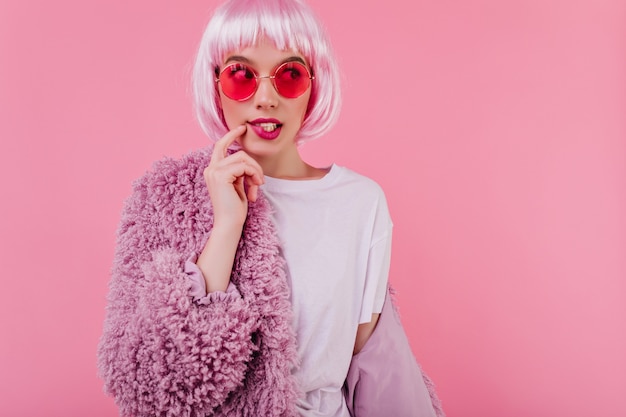 Foto grátis linda garota fashionbale em óculos de sol, posando na parede rosa com casaco de pele. jocund, elegante senhora de peruca se divertindo na sessão de fotos