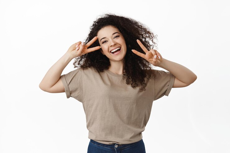 Foto grátis linda garota feliz curtindo a vida, mostrando paz v-sign e rindo despreocupada, de pé otimista contra fundo branco