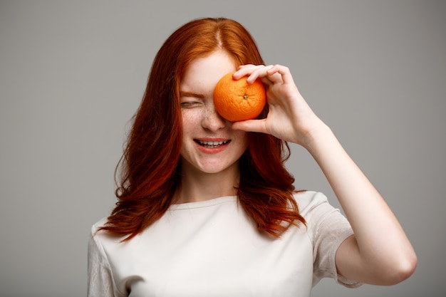 Linda garota gengibre segurando laranja muro cinzento.