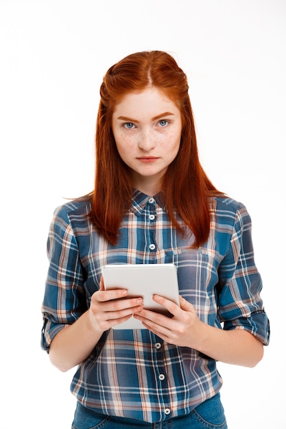 Foto grátis linda garota gengibre segurando o tablet sobre parede branca.