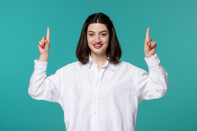 Linda garota jovem morena adorável de camisa branca apontando para cima muito animada