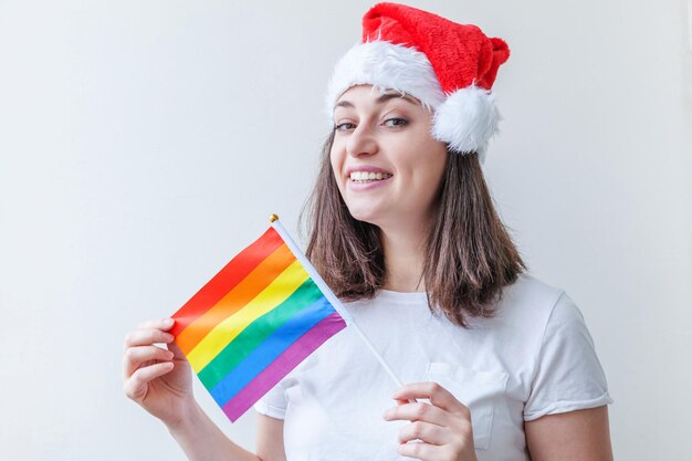 Linda garota lésbica com chapéu de papai noel vermelho com bandeira de arco-íris lgbt isolada no fundo branco ...