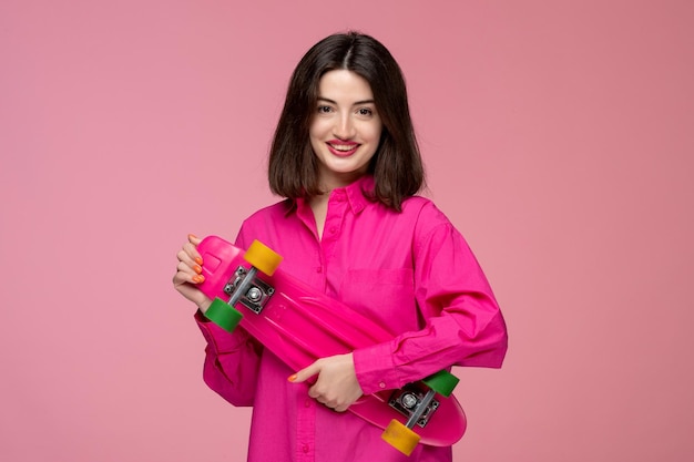 Foto grátis linda garota linda jovem morena de camisa rosa com batom vermelho segurando um skate brilhante