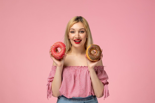 Linda garota loira adorável com batom vermelho na blusa rosa feliz sorrindo com donuts