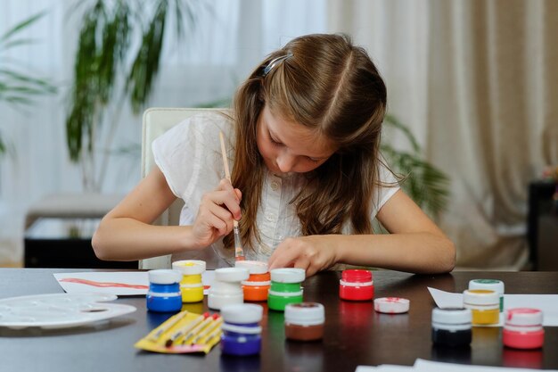 Linda garota loira pintando com tinta acrílica na aula de estúdio de arte.