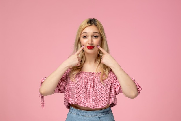 Foto grátis linda garota loira usando batom vermelho em blusa rosa segurando bochechas parecendo doce